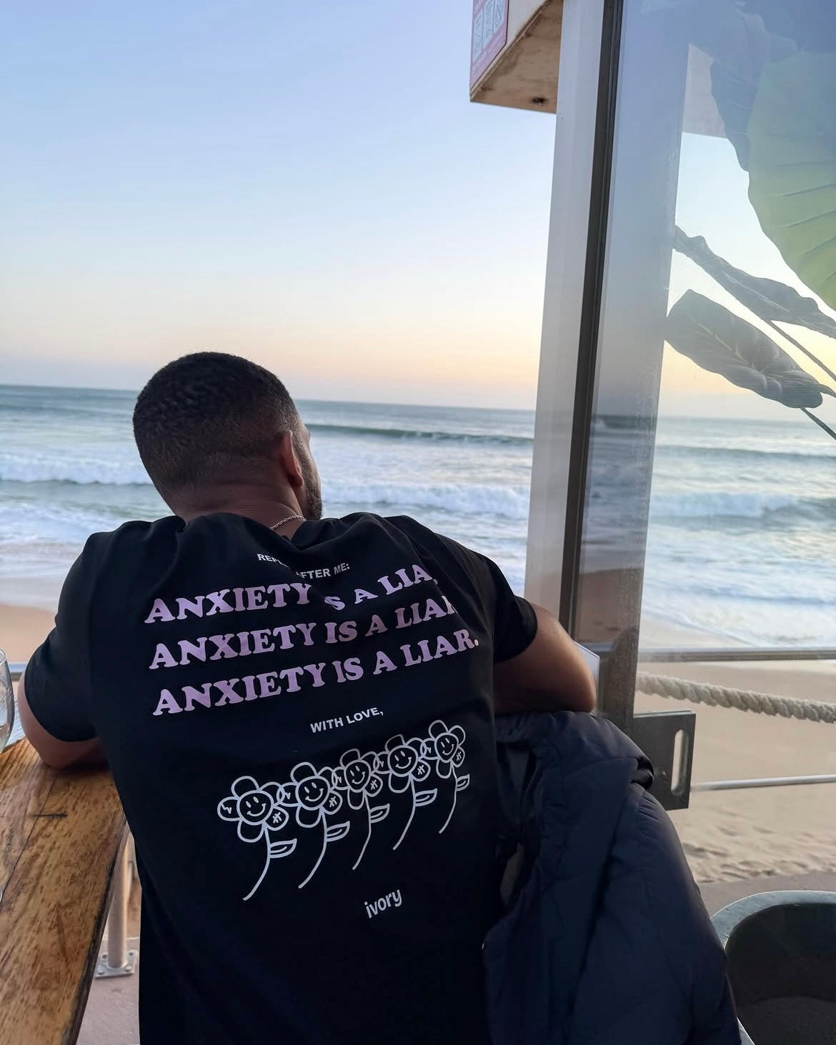 A person wearing an Ivory anxiety awareness T-shirt beside the ocean